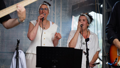 Zwei Sängerinnen singen in festlich weißer Kleidung auf der Konzertbühne während eines Konzerts beim Sommerfest 2026 auf dem Gesundheitscampus Volksdorf des Evangelischen Amalie Sieveking Krankenhauses, der Residenz am Wiesenkamp, des Feierabendhauses Volksdorf und der Albertinen Kindertagesstätte Volksdorf. 