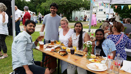 Mehrere Mitarbeitende sitzen um eine im Freien aufgestellte Bierbank mit Essen, Getränken und Blumenschmuck beim Sommerfest 2026 auf dem Gesundheitscampus Volksdorf des Evangelischen Amalie Sieveking Krankenhauses, der Residenz am Wiesenkamp, des Feierabendhauses Volksdorf und der Albertinen Kindertagesstätte Volksdorf. 