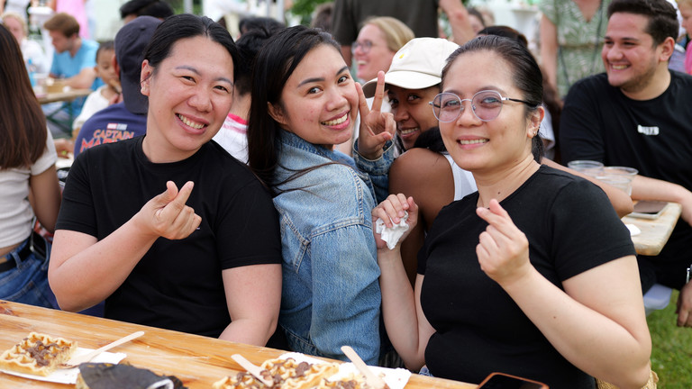 Drei Mitarbeiterinnen sitzen an einem Tisch mit Essenstellern und blicken fröhlich in die Kamera beim Sommerfest 2026 auf dem Gesundheitscampus Volksdorf der Einrichtungen des Evangelischen Amalie Sieveking Krankenhauses, der Residenz am Wiesenkamp, des Feierabendhauses Volksdorf und der Albertinen Kindertagesstätte Volksdorf.