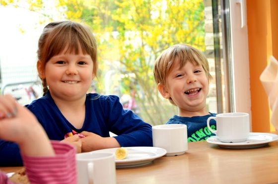 Zwei Kinder sitzen am Tisch und essen etwas, Speiseversorgung in der Kita, Kita-Mahlzeiten, Mittagessen im Kindergarten, Albertinen Kita Volksdorf in Hamburg